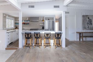 Uma cozinha moderna com armários brancos, uma ilha central com banquetas e uma geladeira de aço inoxidável.