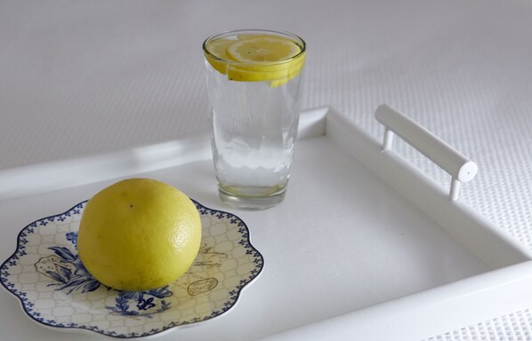 A white tray with a glass of water and a lemon on a decorative plate.