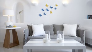 Un saló modern amb un sofà gris, coixinets blancs, una taula de centre blanca amb espelmes, una petita taula auxiliar amb una làmpada i decoracions de papallones penjades a la paret.