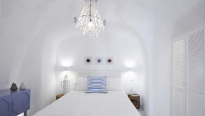 Una habitació blanca amb un llit, un penjador, un taulell i un armari.