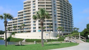 Un hotel de varios pisos con balcones, una palmera y una fuente de agua.