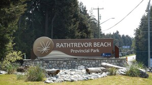A sign for Rathtrevor Beach Provincial Park with a stone wall and rocks in the foreground.