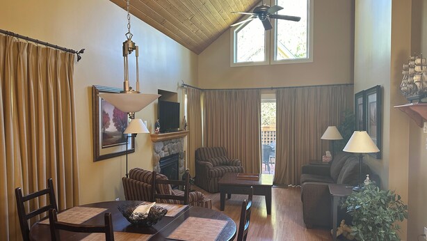 A spacious living room with a fireplace, dining area, and a large window with curtains.