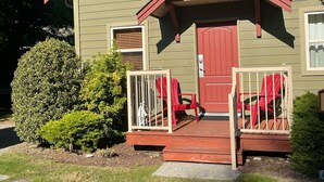 A two-story house with a red door and a small porch with red chairs.