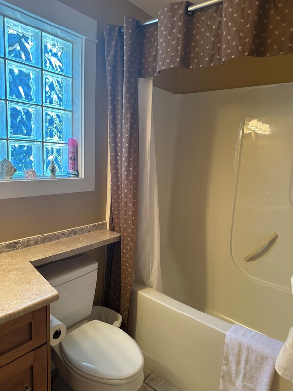 A bathroom with a toilet, a bathtub, a window with a view of the sea, and a shower curtain.