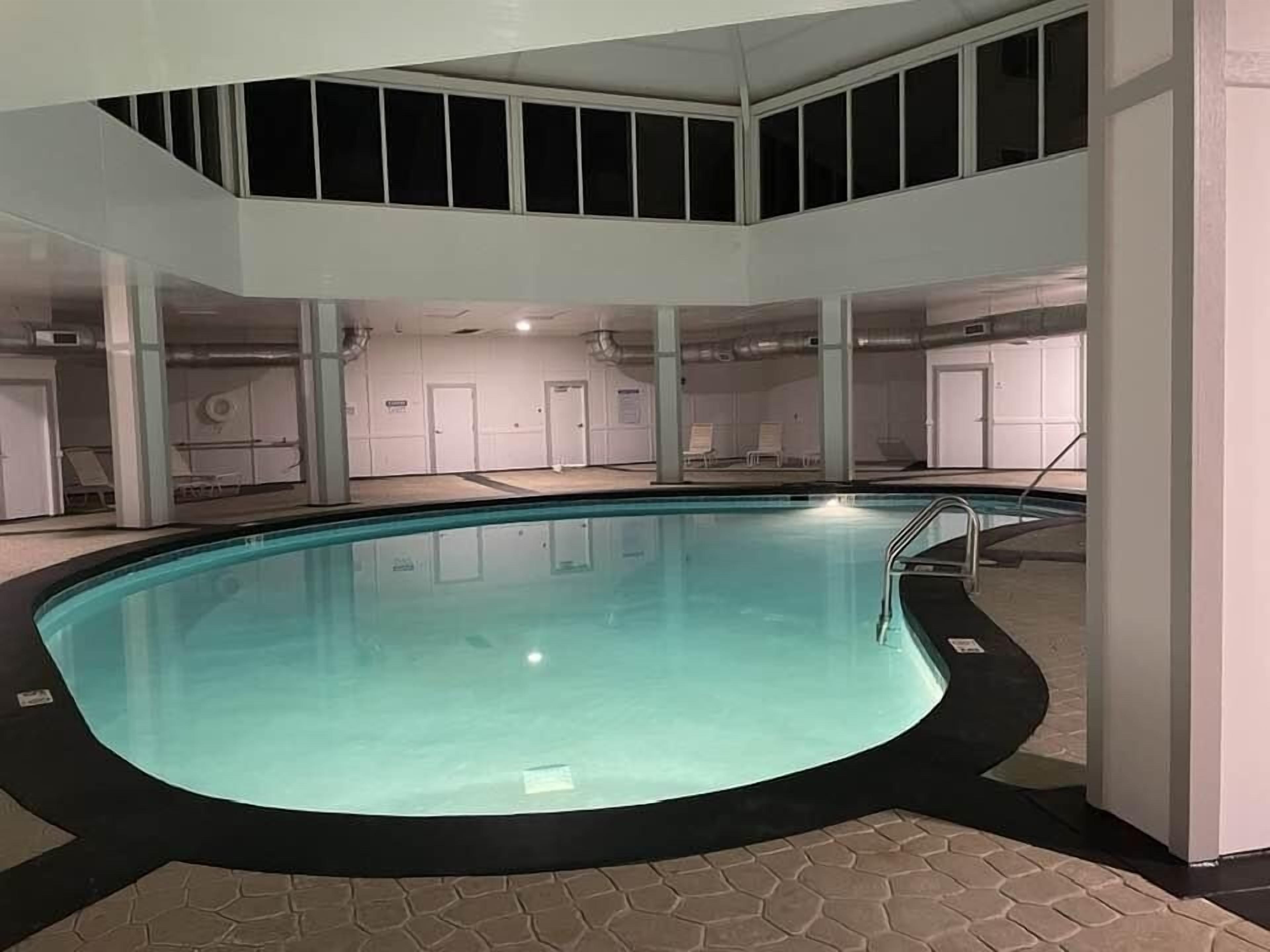 Una piscina interior con suelo de baldosas y borde negro. Se observan varias puertas y ventanas al fondo.