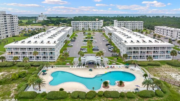 Et moderne hotelkompleks bestående af flere bygninger, en central swimmingpool og en parkeringsplads.