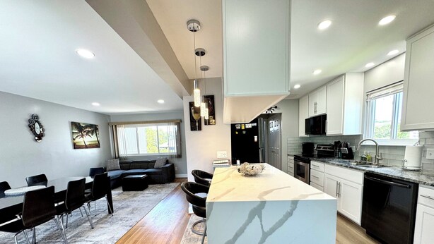A modern kitchen with white cabinets, a central island, and a dining area with a sofa and chairs.