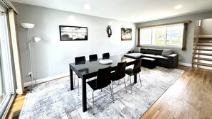 A modern living room with a dining table, chairs, a sofa, and a staircase.