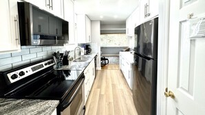 A modern kitchen with white cabinetry, a black stove, and a stainless steel refrigerator.
