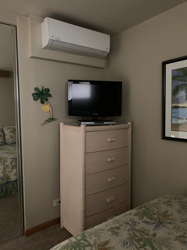 Un dormitorio con una televisión sobre un tocador, un cuadro en la pared y una puerta que da a otra habitación.