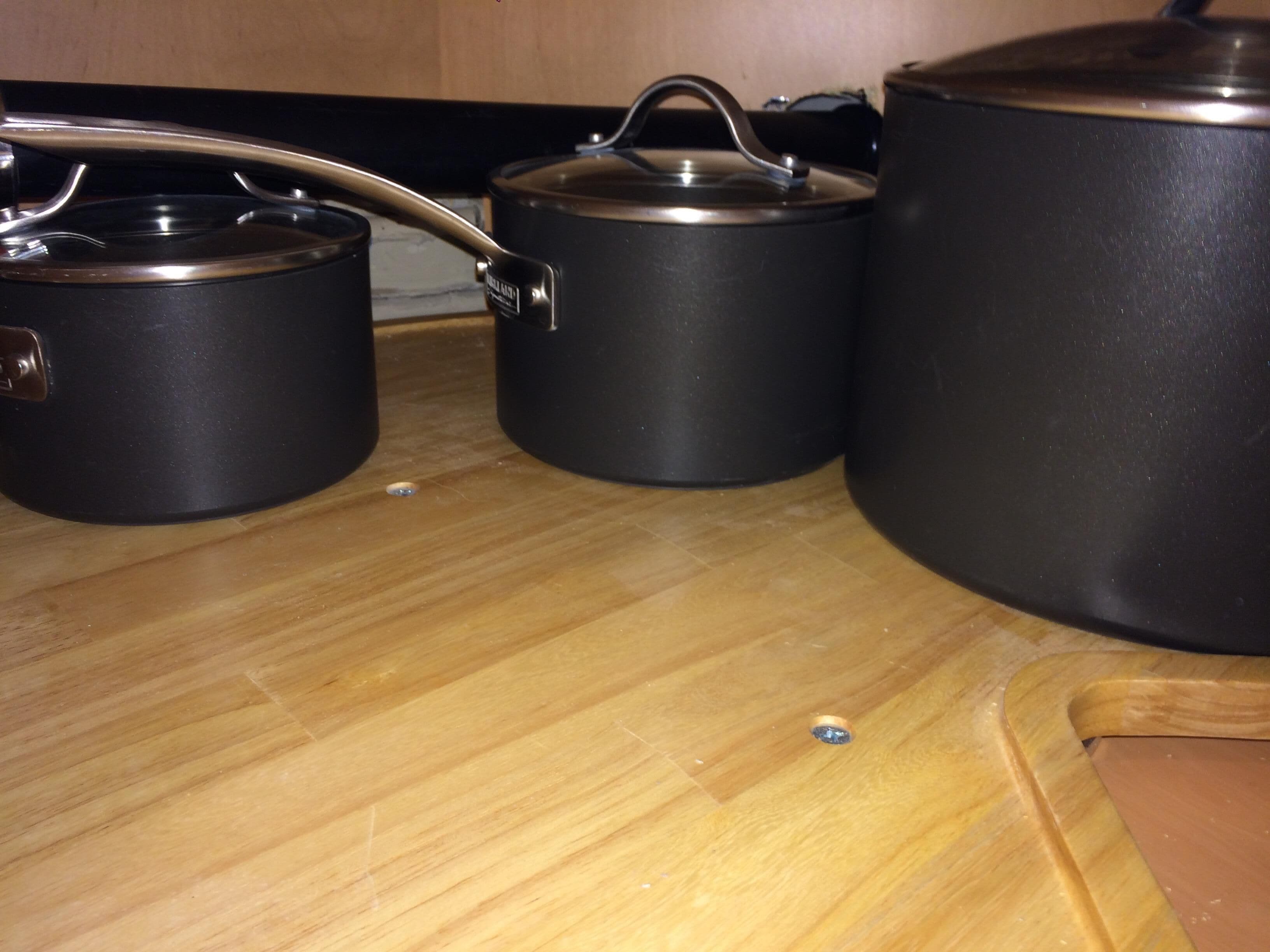 Three black pots on a wooden countertop.
