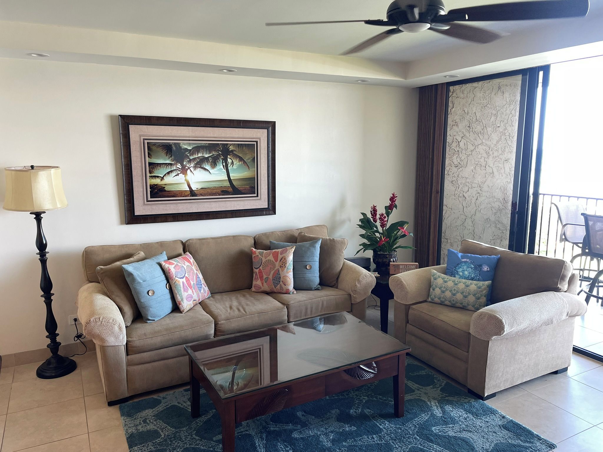 A living room with a sofa, armchairs, a coffee table, a lamp, a framed picture, and a balcony with a view.