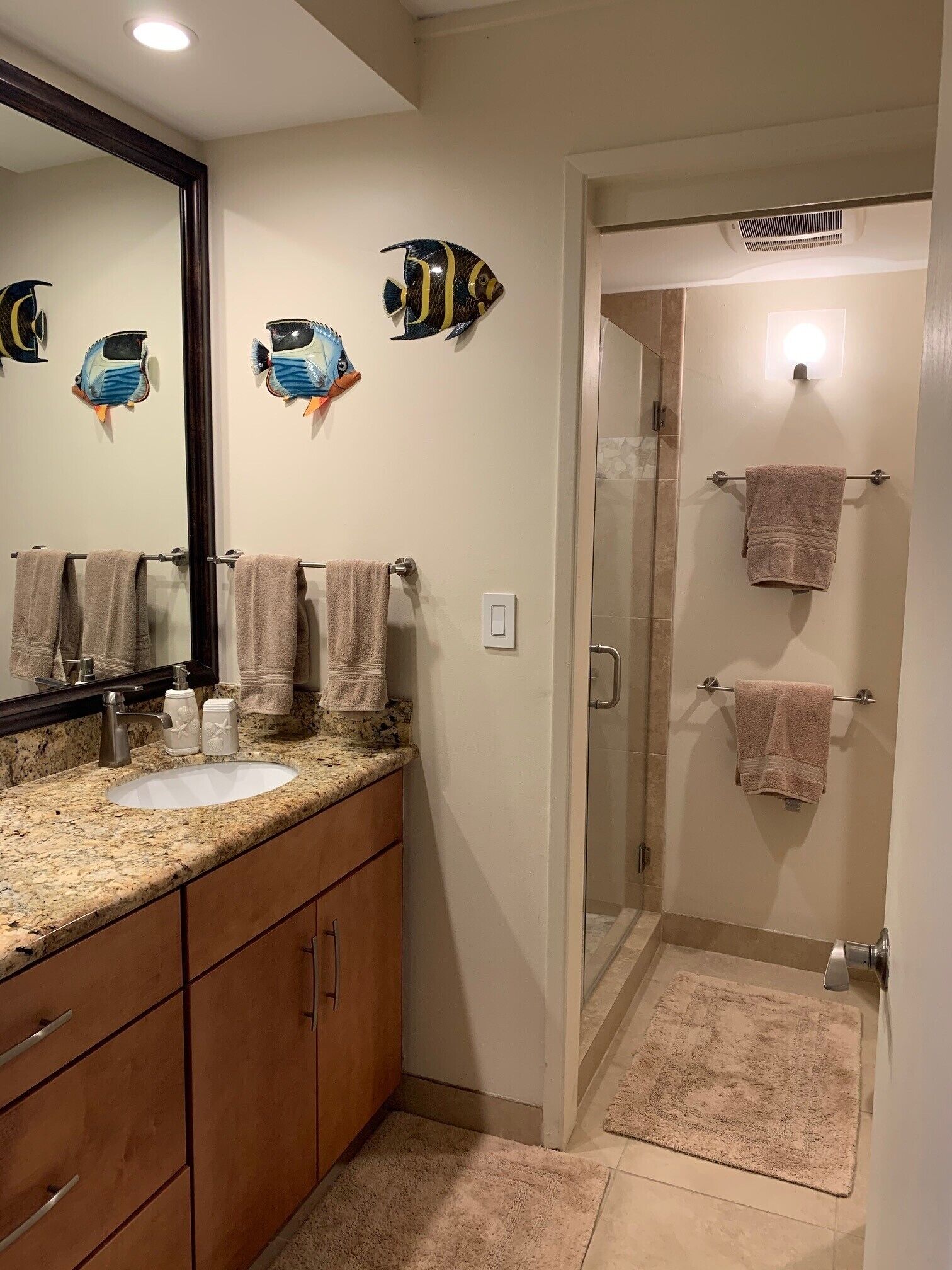 A bathroom with a granite countertop, two sinks, a mirror, and decorative fish wall art.