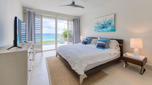 A bedroom with a bed, a TV, a desk, a nightstand, and a ceiling fan. - Villa Amaya - Modern, Pristine Villa, Stunning Ocean Views, Private Pool, Beach (Indigo Bay)