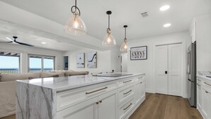 A modern kitchen with white cabinetry, a marble island, pendant lighting, and a view to the outside.
