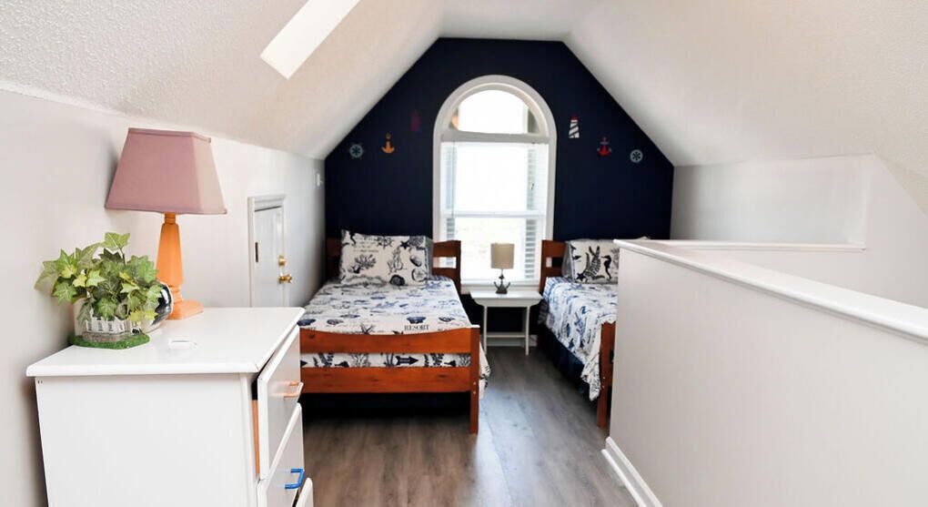 Un dormitorio con techo inclinado, un escritorio con lámpara, dos camas con ropa de cama estampada y una ventana con vistas.