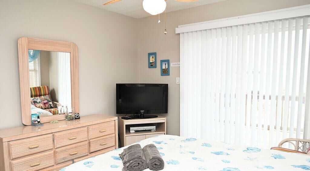 Ein Schlafzimmer mit einem Bett, einem Schminktisch, einem Fernseher und einem Fenster mit Jalousien.