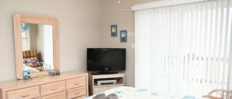 Ein Schlafzimmer mit einem Bett, einem Schminktisch, einem Fernseher und einem Fenster mit Jalousien.