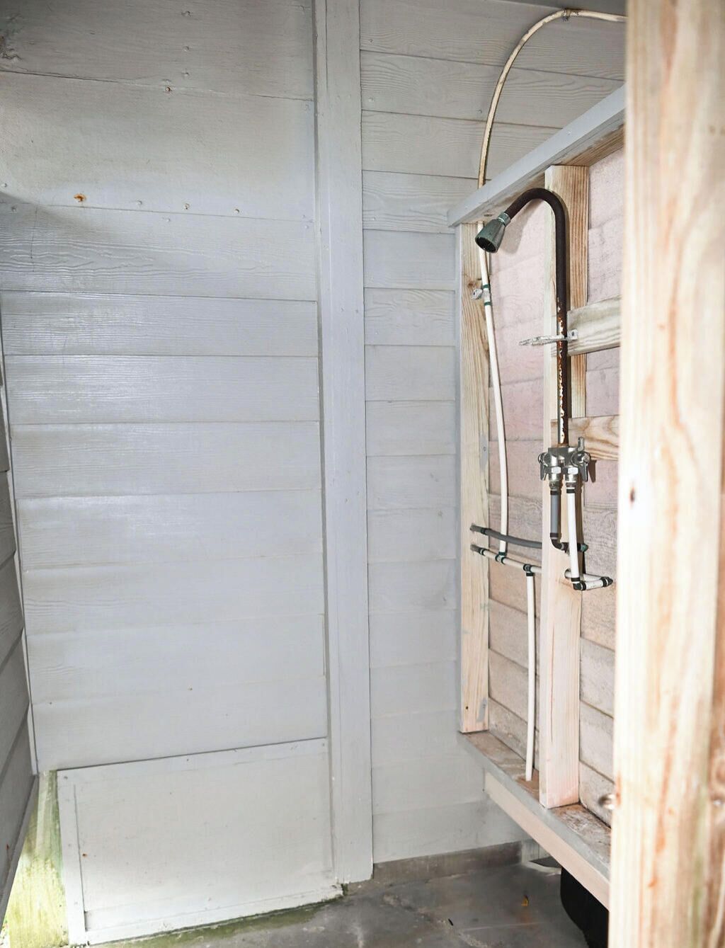 Une salle de bain avec un meuble-lavabo en bois, une douche avec un flexible et un système de tuyauterie apparent.