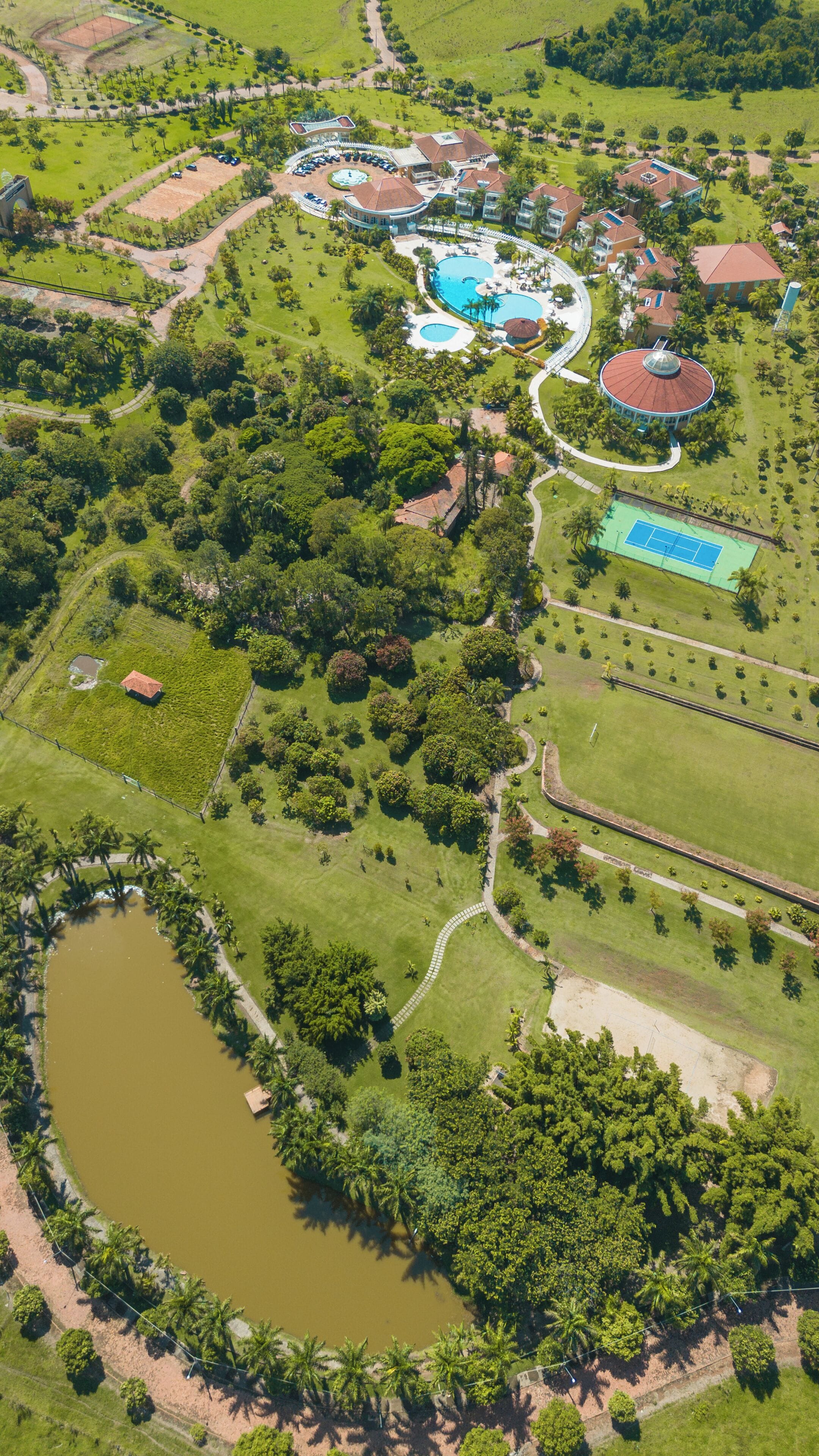Vista aérea de um resort com piscina, quadras de tênis e um lago grande.