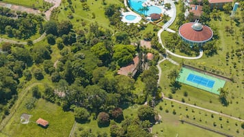 Vista aérea de um resort com piscina, quadras de tênis e um lago grande.