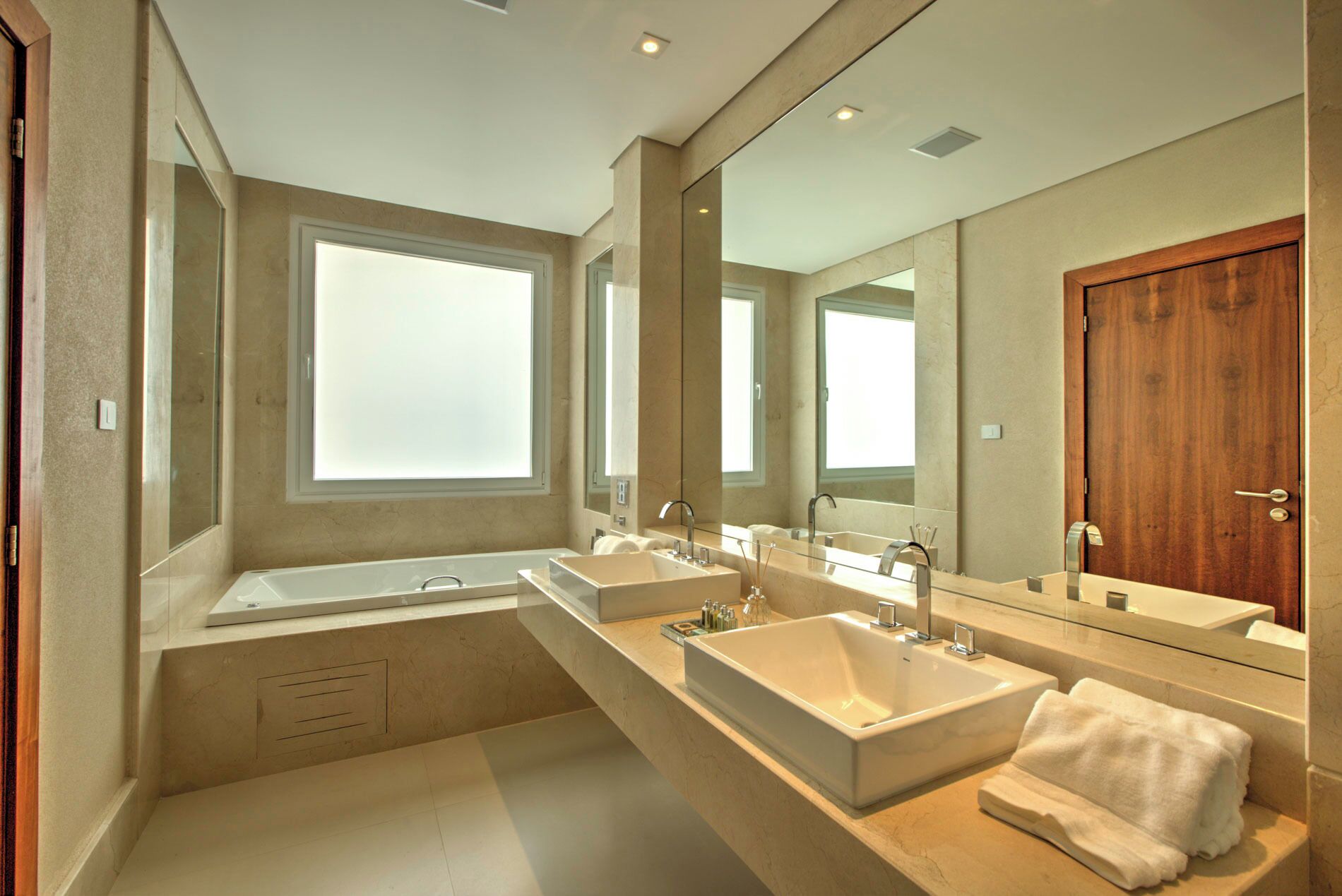 Une salle de bain moderne dotée d’une grande fenêtre, d’une porte en bois et d’un long meuble-lavabo avec deux vasques.