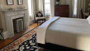 A bedroom with a large bed, a fireplace, a chair, a dresser, and a potted plant. - Historic Home At Freedom Trail (Boston)