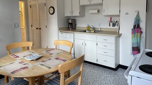 A compact kitchen with white cabinets, a dining table set for four, a coffee maker, and a stove. - Historic Home At Freedom Trail (Boston)