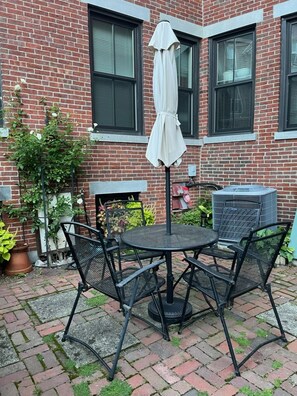 A brick building with a patio area featuring a round table with four chairs and a white umbrella. - Historic Home At Freedom Trail (Boston)