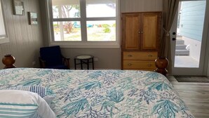 A bedroom with a bed, a chair, a small table, a wardrobe, and a window with a view of the outside. - Paradise Beach Cottage- Newly Renovated 3 Bed/3 Bath Cottage On The Beach (Eleuthera)