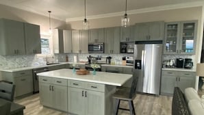 A modern kitchen with grey cabinets, a central island, stainless steel appliances, and pendant lighting. - Paradise Beach Cottage- Newly Renovated 3 Bed/3 Bath Cottage On The Beach (Eleuthera)
