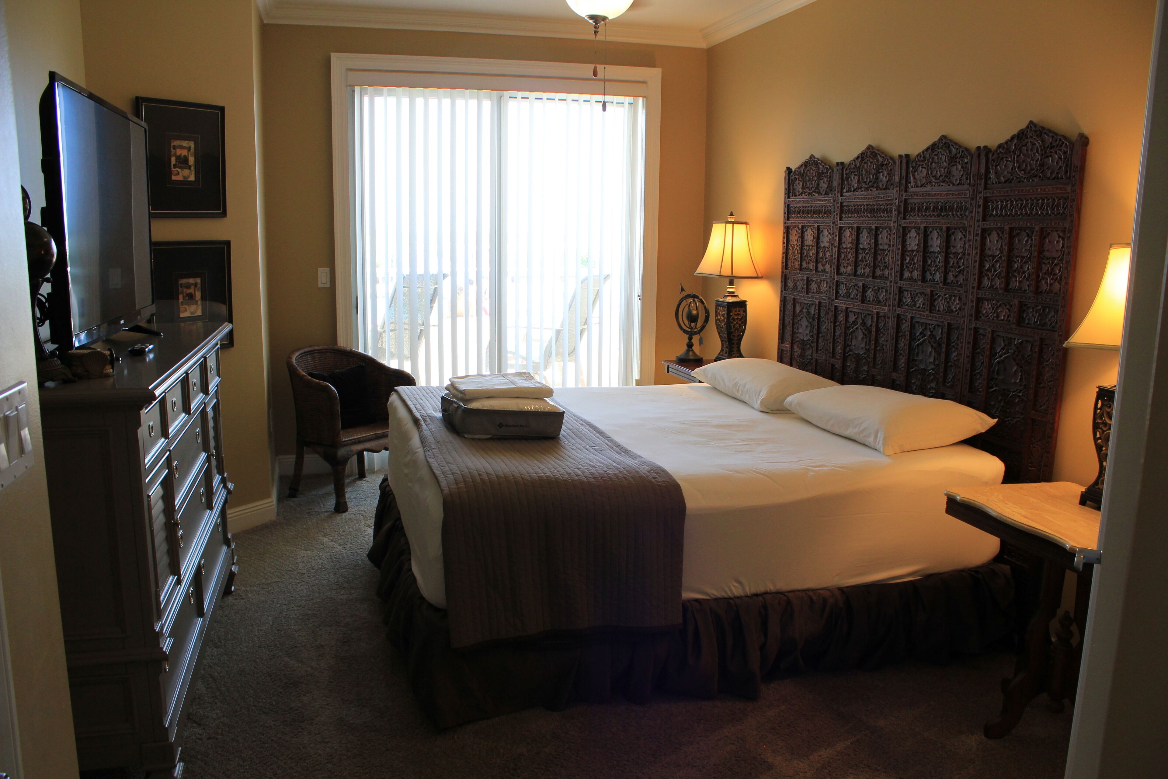 A hotel room with a large bed, a dresser, a television, and a window with blinds.