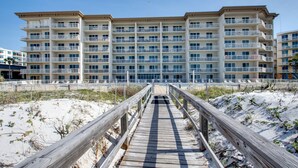 Un hotel de diversos pisos amb balcons, una passera de fusta que condueix a l'entrada i una platja sorrenca al fons.