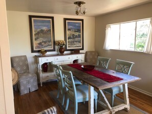 A dining room with a wooden table, six chairs, a vase with flowers, and two framed paintings on the wall. - Escape to Tranquility: Your Private Oasis Awaits (Carmel)