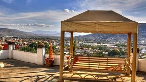Une terrasse sur le toit, avec un banc en bois et un auvent, d’où l’on peut admirer un panorama urbain avec des montagnes à l’horizon.