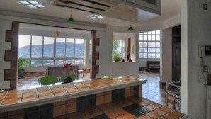 Une pièce spacieuse dotée d’une grande fenêtre donnant sur les montagnes, d’un sol carrelé et d’une longue table à manger.