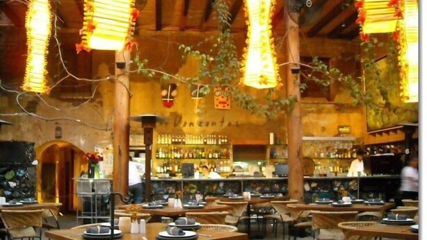 Un espace de restauration intérieur avec des tables et des chaises, un bar en arrière-plan et des luminaires suspendus.