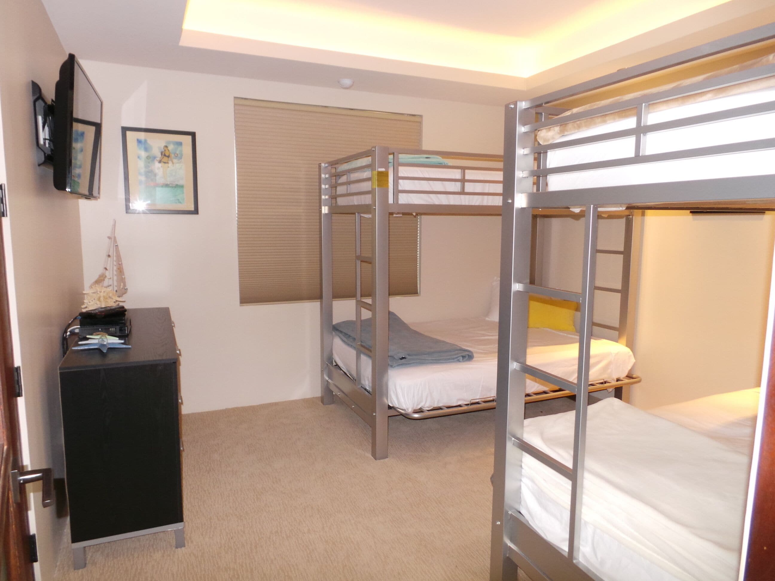 Une chambre avec un lit superposé, un bureau et une fenêtre avec des stores.