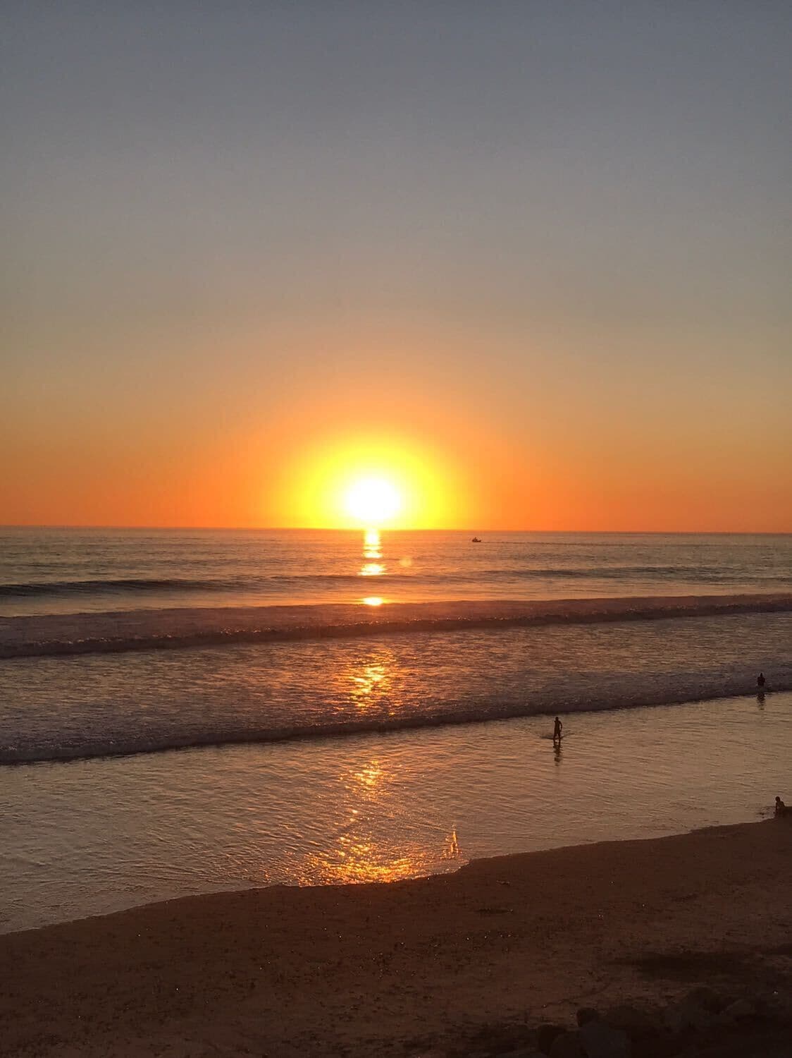A sunset over the ocean with waves gently lapping onto the shore.