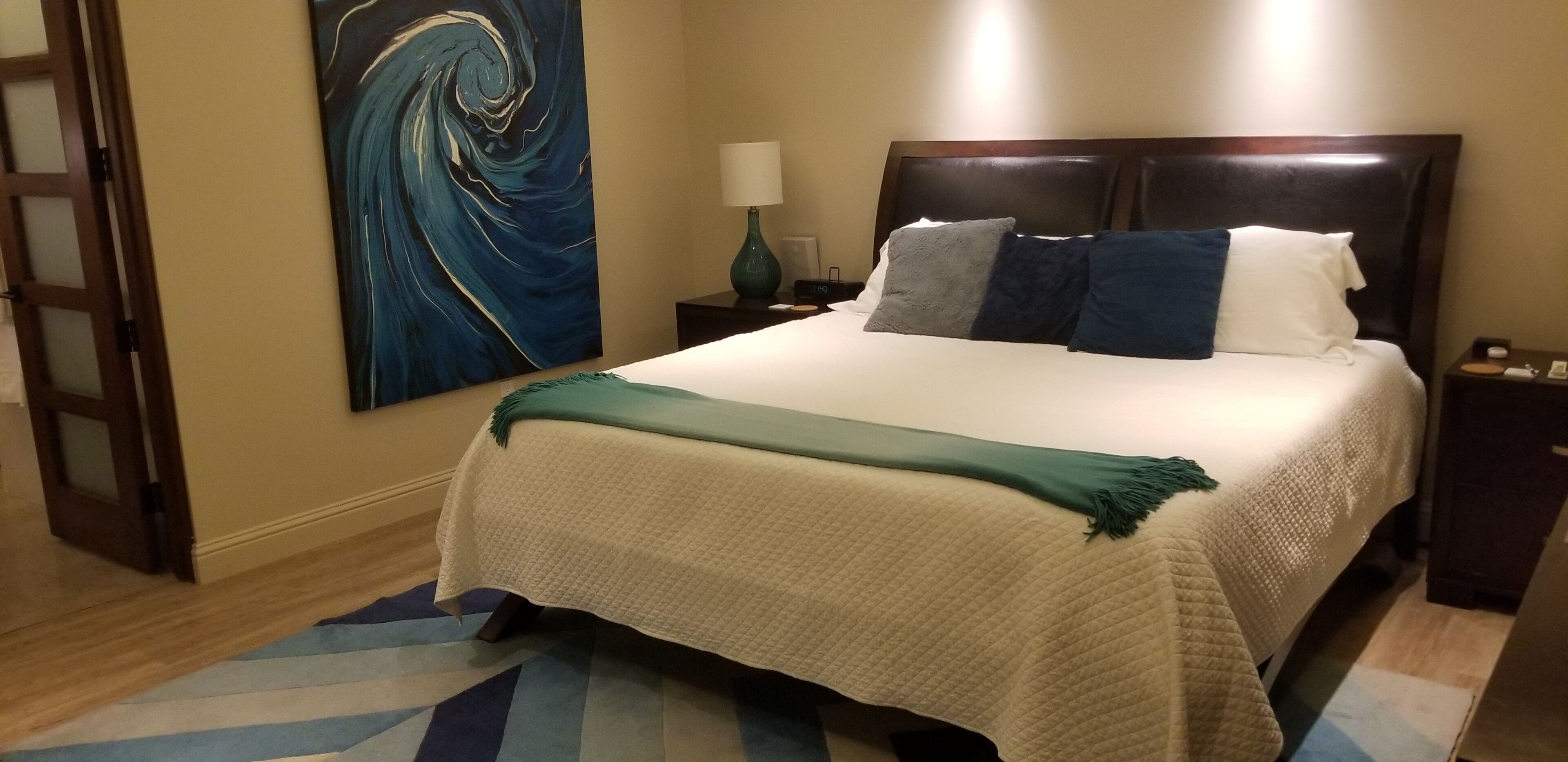 A hotel room with a bed, a nightstand, a lamp, and a painting on the wall.