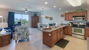 A modern kitchen with wooden cabinets, a central island, and a dining area with blue furniture. - Beautiful Beach View Condo!  1 Bedroom, Bunk room and 2 bath (Miramar Beach)