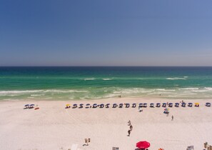 Une plage de sable blanc, sous un ciel bleu azur. On y voit des parasols et des gens.