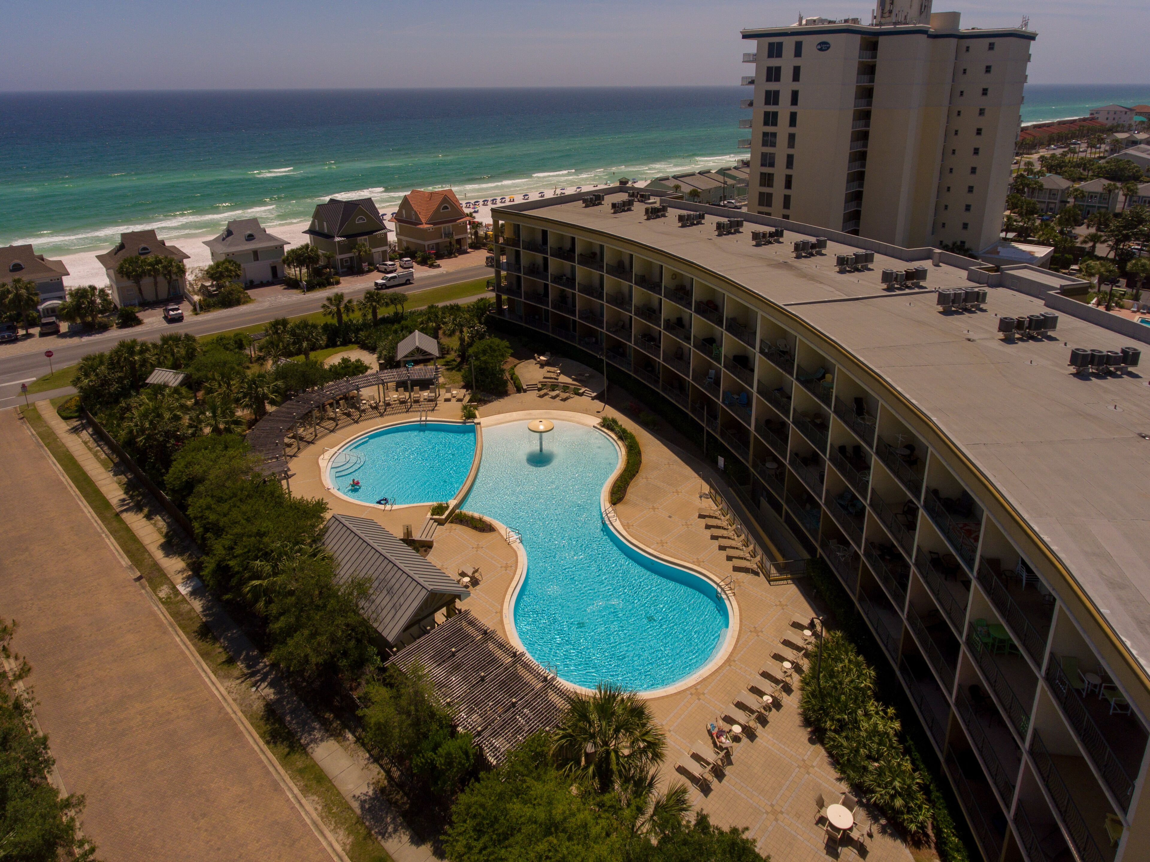 A hotel with a large pool, a beach view, and a high-rise building in the background.