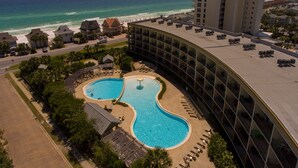 A hotel with a large pool, a beach view, and a high-rise building in the background. - Beautiful Beach View Condo!  1 Bedroom, Bunk room and 2 bath (Miramar Beach)