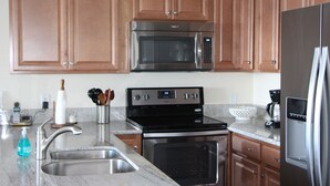 A kitchen with wooden cabinets, stainless steel appliances including a microwave, oven, and refrigerator, a marble countertop, and a sink. - Oceanfront 2 BR/2BA in Beautiful Sea Village. (Kailua-Kona)