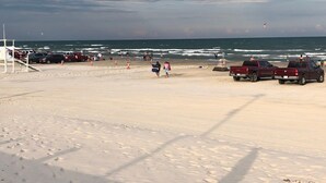 Una playa con arena, algunas personas y vehículos estacionados.