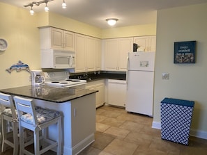 Kitchen features a microwave, stove, and dishwasher, along with two bar stools and a framed quote on the wall.