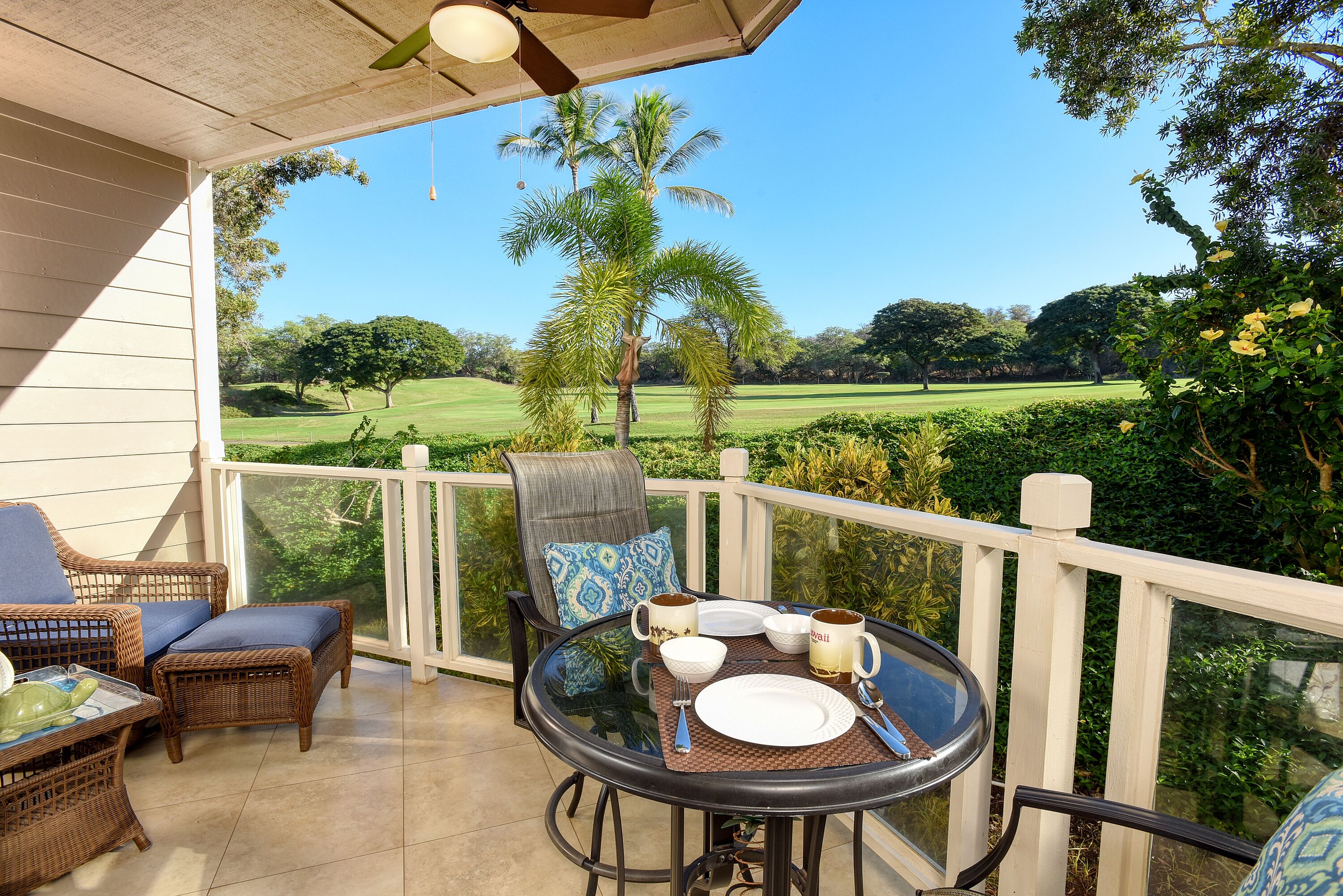 A covered outdoor seating area with wicker furniture, a glass table, and a view of a golf course.