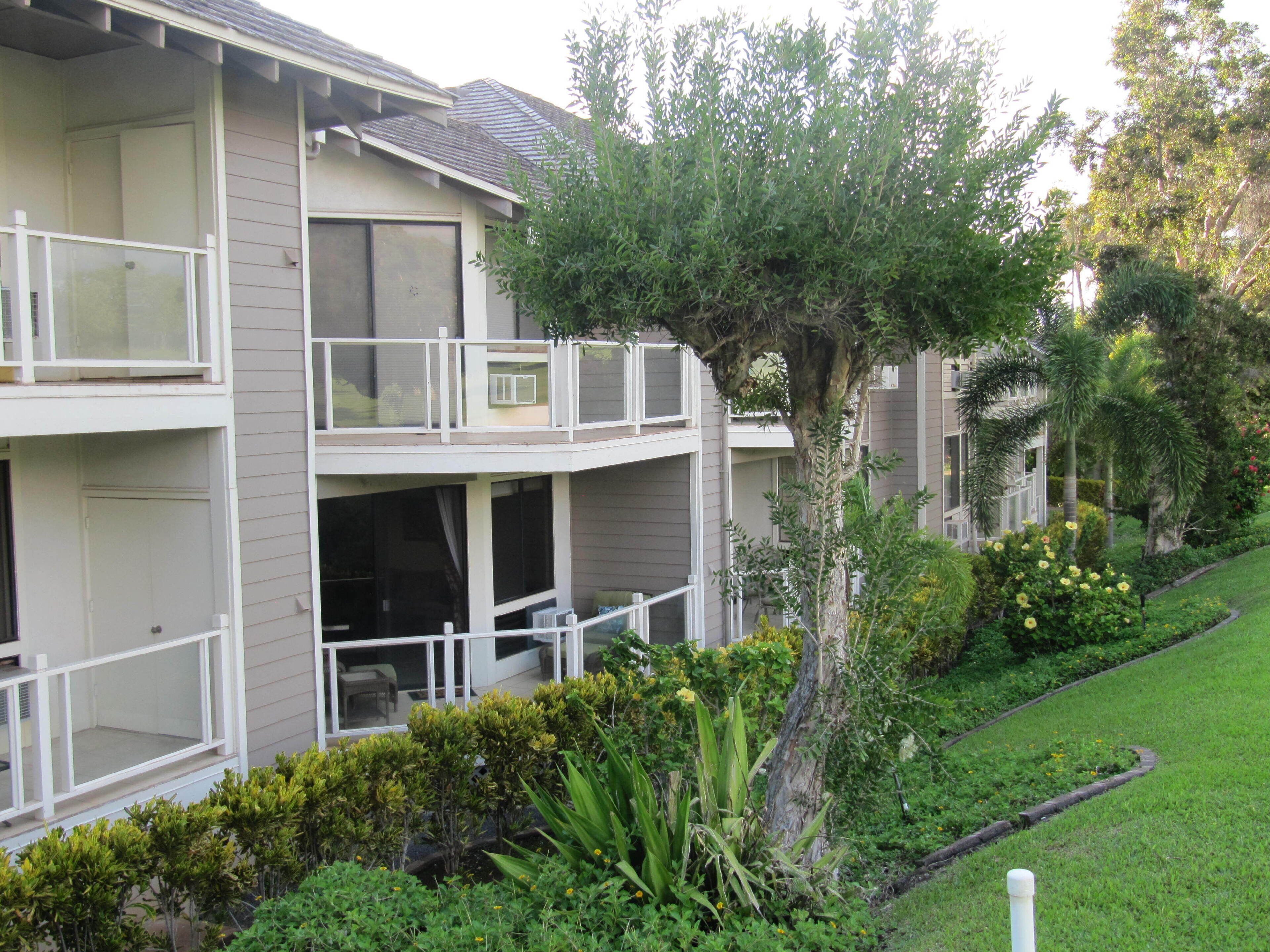 A multi-story residential building with balconies, a well-maintained lawn, and various shrubs and trees.